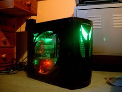 3/4 portrait view of the full PC with all lighting elements turned on: bright green frontal lighting, green internal lighting for the hardware components ans amber internal lighting for the diorama